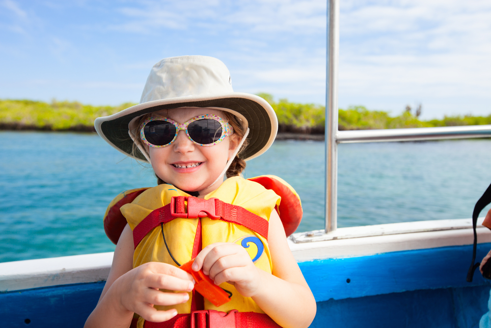 Summer Vacation Safety Tips.  Adorable little girl in a life jacket travelling on boat.