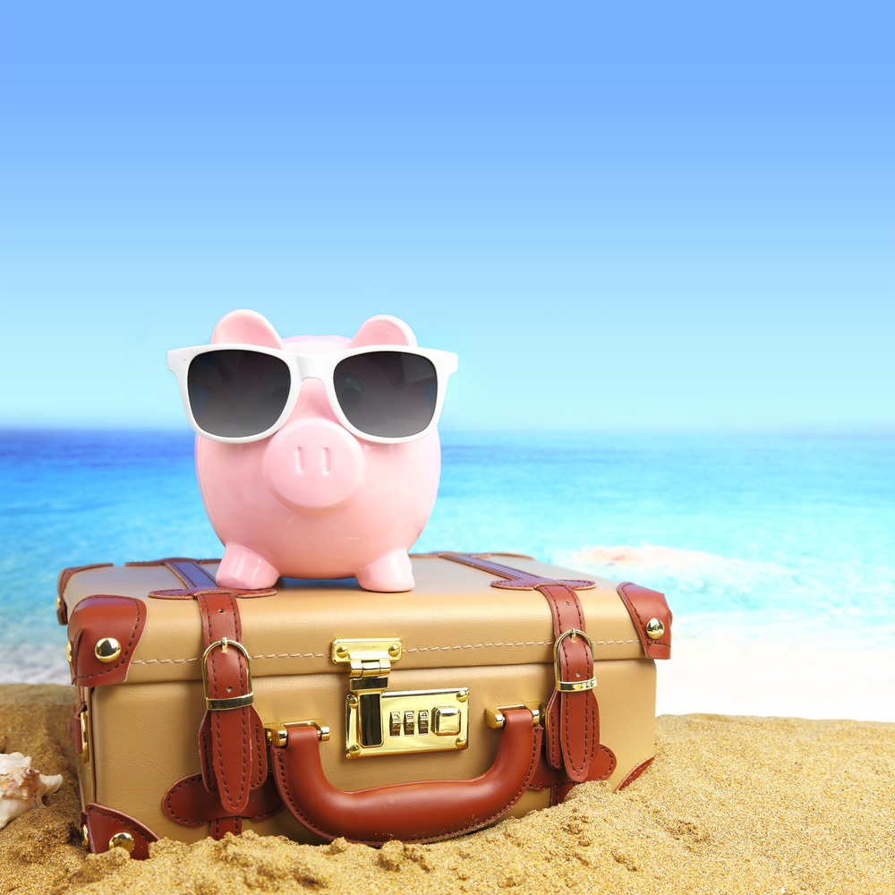 Suitcase with piggy bank in sunglasses on tropical beach.
How to build a travel fund.