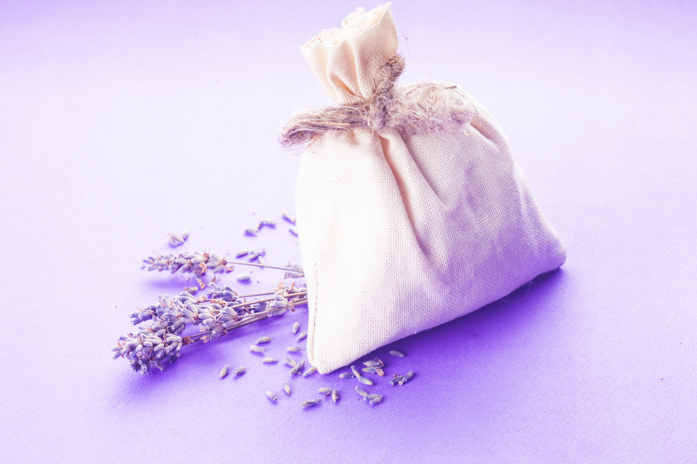 How to sleep on vacation with aromatherapy. Dried lavender sachet over purple background with flowers 