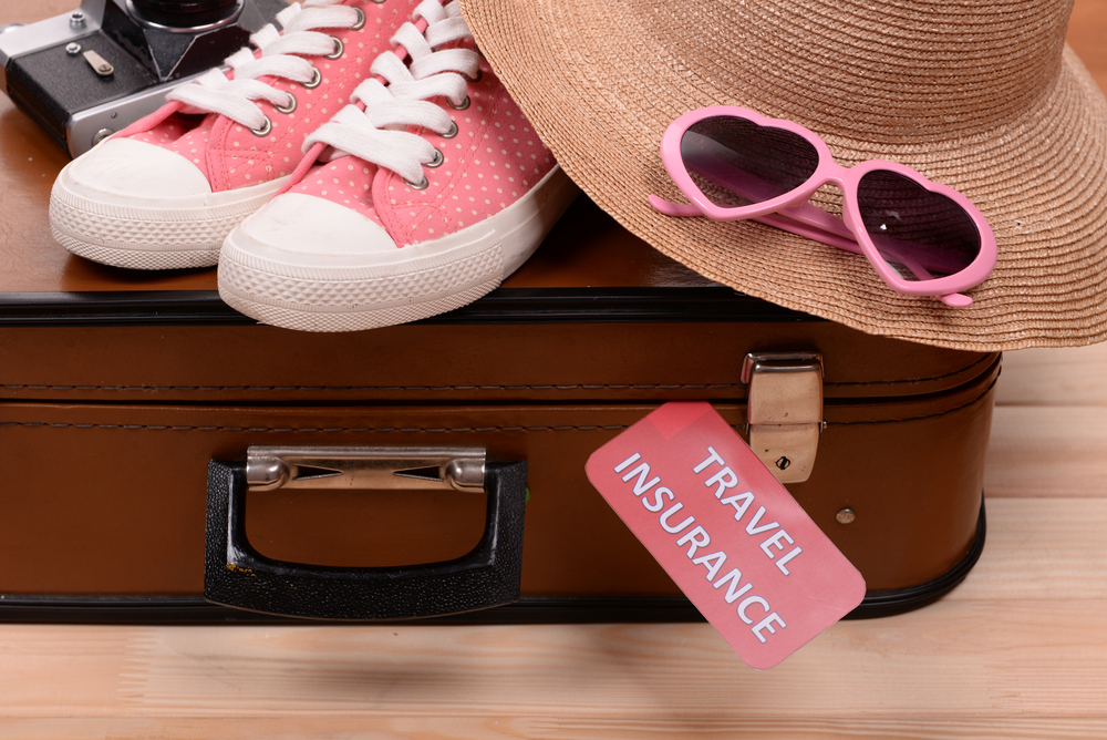 Pre-Travel Checklist.
Suitcase and tourist stuff with inscription travel insurance on wooden background