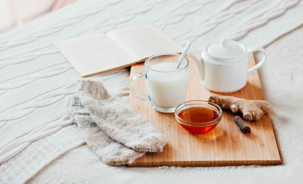 How to Get Over Jet Lag.
Hot milk in a glass cup and honey on a wooden board. Treatment of children a hot drink. Treatment of folk remedies in bed. Warm knitted socks. The book to read.