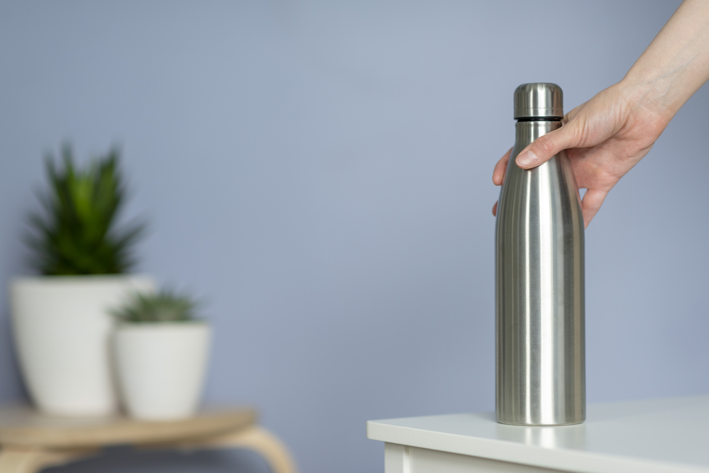Eco-Friendly Travel Products.
Woman hold steel water bottle on the table at home. 