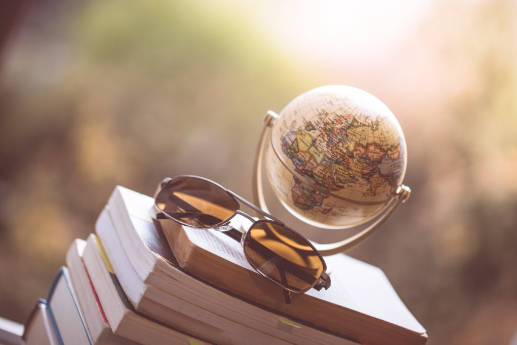 Books About Travel and Self-Discovery.
Miniature globe model and sunglasses lying on a stack of books. Symbol for travelling.
