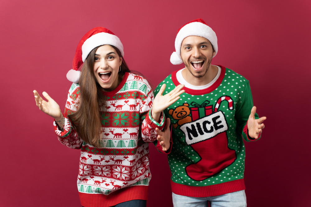 Christmas Bucket List Ideas.
Hispanic couple wearing ugly sweaters and looking shocked while looking at an amazing Christmas deal
