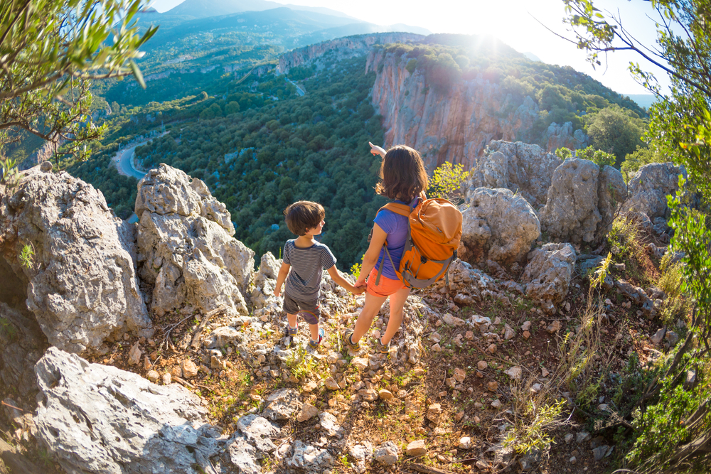Family Travel Tips.  The boy and his mother are standing on the top of the mountain, A woman is traveling with child, Boy with his mother looking at the mountains, Travel with backpacks, Hike and climb with kids.